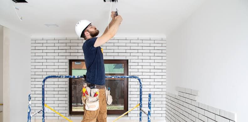 Electricista con casco blanco trabajando en el techo de una vivienda subido a un andamio
