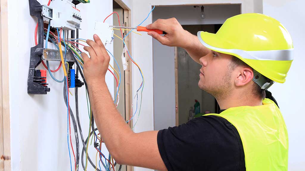 Electricista con casco amarillo conectando los cables de un cuadro eléctrico con un destornillador